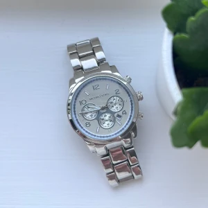 Silverfärgad klocka - Snygg och stilren silverfärgad klocka med metallarmband och flera små urtavlor. Perfekt för att hålla koll på tiden med stil. Klockan har en klassisk design som passar till många tillfällen. Sparsamt använd. Måste ha nytt batteri! Önskar du veta exakta mått? Tveka inte att höra av dig!