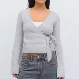 Grå omlottkofta - Säljer en mysig grå omlottkofta med knytning i sidan. Koftan har en v-ringad design och långa breda ärmar. Från Gina Tricot i strl xs. Nytt skick