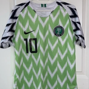 Grön och vit fotbollströja från Nike - Säljer en grön och vit fotbollströja från Nike med ett zigzag-mönster. Tröjan har korta ärmar och ett svart nummer 10 på framsidan. Perfekt för fotbollsfans som vill sticka ut på planen!