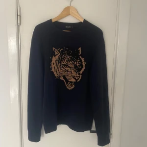 Mörkblå stickad tröja från Tiger of Sweden - Säljer en mörkblå tröja från Tiger of Sweden med ett coolt tryck på framsidan. Tröjan har långa ärmar och en rund halsringning. Perfekt för en stilren och djärv look. Passar M bra! Skriv om ni har några övriga frågor🙌