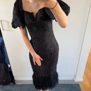Klänning  - Elegant svart klänning med spetsdetaljer och puffiga kortärmar. Den har en figurnära passform och en unik fåll med fransar. Perfekt för en kväll ute eller en speciell tillställning. Aldrig använt innan! Prislappen sitter på 