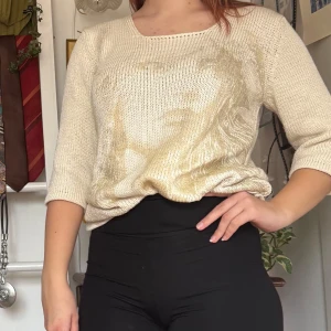 Off-white stickad tröja med motiv - Köpt second hand och använt en del. Säljer en off-white stickad tröja med ett subtilt motiv i guld på framsidan. Tröjan har trekvartsärmar och en rund halsringning. Perfekt för en avslappnad stil.