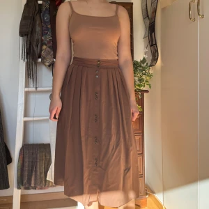 Brun klänning med knappar - Köpt secondhand och använd en del. Säljer en stilren brun kjol med knappar framtill. 