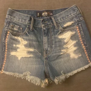 Snygga Jeansshorts ifrån Hollister🌺🩷 - Snygga jeansshorts från Hollister med slitna detaljer och fransar. De har dekorativa sömmar i orange längs sidorna vilket gör dem extra unika! Perfekta nu inför sommaren!☀️🍓 (Frakt tillkommer)