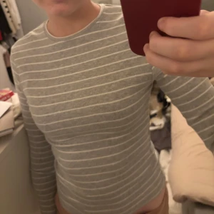 Grå och vit randig tröja - Säljer en grå och vit randig tröja med långa ärmar.  Tröjan har en rund halsringning och är tillverkad i ett mjukt material.