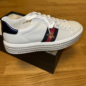 Gucci Sneakers med diamanter - Vita sneakers från Gucci med ikoniska ränder i rött och blått samt diamanter med guldbroderat bi. Skorna är aldrig använda eller prövade, dom är köpta av mig från Gucci butiken i Italien, Florens. Som man ser på bilden har jag kvitto/äkthetsintyg. Skriv om du har frågor eller ett bud 😊. Kommer jag ihåg rätt ligger nypris runt 1100 euro så 11.500kr. Jag köpte dom åt min flickvän men fick inte möjlighet att ge henne dom.