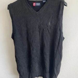 Svart v-ringad väst från Chaps - Säljer en klassisk svart v-ringad väst från Chaps. Västen är tillverkad i bomull och har ribbade kanter. Perfekt för lager-på-lager-stil eller som ett stilrent tillskott till garderoben.