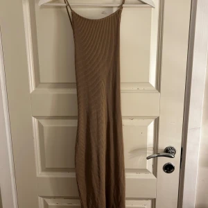 Beige ribbad långklänning - Säljer en stilren beige ribbad långklänning med smala axelband och snygg snörning i ryggen. Perfekt för en avslappnad och chic look. Passar bra till både vardag och festliga tillfällen.