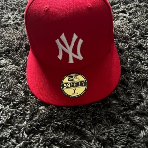 Röd keps med vit broderad logotyp - Snygg röd keps från New Era med en vit broderad logotyp på framsidan. Kepsen har en platt skärm och är en del av 59FIFTY-serien. Perfekt för att ge din outfit en sportig touch. Pris kan diskuteras!