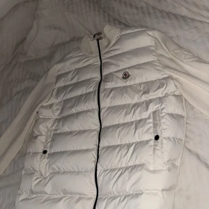 Vit cardigan från Moncler - Snygg vit pufferjacka från Moncler med stickade ärmar och dragkedja framtill. Jackan har en quiltad design och två fickor med knappar. Perfekt för kyligare dagar.Storlek L - XL