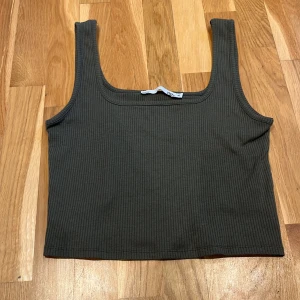 Olivgrön ribbad linnetopp  - Säljer en olivgrön ribbad linnetopp från Lager 157 i storlek XL. Toppen har en enkel och stilren design med breda axelband och en rundad halsringning. Perfekt för en avslappnad look!