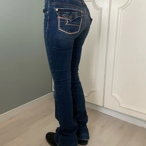 Mörkblå bootcut jeans - Snygga mörkblå bootcut jeans med vintage dekorativa sömmar på bakfickorna. Från American eagle strl 0. Midjemått 34 cm Grenmått 26 cm  innebenslängd 83 cm