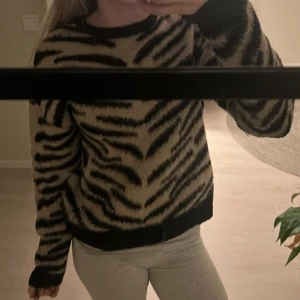 Zebramönstrad tröja från NA-KD - Säljer en cool zebramönstrad tröja från NA-KD i beige och svart. Tröjan har långa ärmar och en normal passform, perfekt för att sticka ut i mängden. Den är tillverkad i ett mjukt material som känns skönt mot huden.