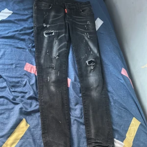 Svarta jeans från Dsquared2 - Snygga svarta jeans från Dsquared2 med slitna detaljer och en cool look. De har en knappgylf och en röd etikett med logotypen. Perfekta för en trendig stil. Passar nog någon som är ungefär 160-165 cm lång.