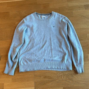 Gant Tröja - Nypris: 1100kr. Säljer en stilren grå tröja från GANT med broderad logga på bröstet. Tröjan har långa ärmar och ribbade kanter vid hals, ärmslut och nederkant. Perfekt för en avslappnad och snygg look.