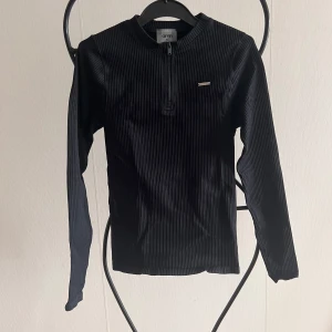 Svart ribbad tröja från Aim'n - Snygg svart ribbad tröja från Aim'n med dragkedja framtill. Perfekt för en stilren look eller att träna i. Tröjan har långa ärmar och en liten logga på bröstet. Aldrig använd, testat några gånger hemma bara. 