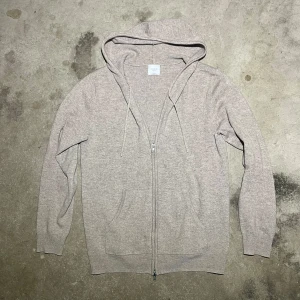 Kashmir hoodie från John Henric - Säljer en lyxig beige hoodie från John Henric i 100% kashmir. Den har en dragkedja framtill och en bekväm huva med snören. Perfekt för att hålla sig varm och stilren. Passar både till avslappnade och mer uppklädda tillfällen. Nypris 2499kr