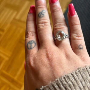 Silverring med stor klar sten - Snygg silverring med en stor, oval klar sten i mitten och detaljerat mönster på ringskenan. Ringen har en elegant och lite bohemisk vibe, perfekt för dig som gillar att sticka ut med dina accessoarer.