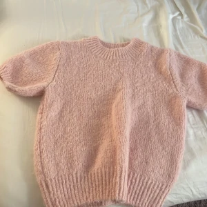 Rosa stickad tröja från Gina Tricot - Supermjuk och fluffig rosa stickad tröja från Gina Tricot i storlek XS. Tröjan har korta ärmar, rund halsringning och bred ribbad mudd nertill och vid halsen. Perfekt för lager-på-lager och ger en söt vibe till din outfit.