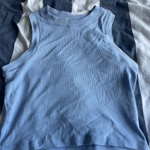 Ljusblå ribbad linnetopp Gina Tricot - Säljer en ljusblå ribbad linnetopp från Gina Tricot. Toppen är ärmlös med hög halsringning och har en tight passform. Säljer då jag inte använder den längre.
