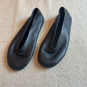 Svarta ballerinaskor i skinn från Khaite - Minimalistiska svarta ballerinaskor från Khaite i mjukt skinn. Skorna har en rund tå och en stilren, avskalad design med låg profil. Tillverkade i Italien och perfekta för dig som gillar en clean och modern look.