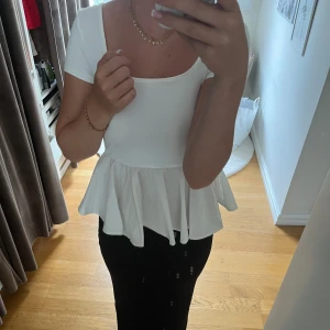 Vit sommartopp med öppen rygg - Säljer en vit T-shirt/top som är super fin! Den sitter tajt upptil och har en vågig detalj nertill. Ryggen är hur snygg som helst med snörningen! 