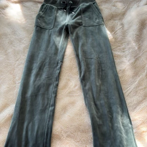 Mörkgröna mjukisbyxor Juicy Couture XS - Mysiga gröna mjukisbyxor från Juicy Couture i perfekt kvalité och snörning i midjan. Byxorna har stora fickor fram och bak med silverfärgade knappar. Perfekta för chill dagar eller när du bara vill mysa.