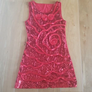 Röd paljettklänning från Liang Li - Supersnygg röd kortklänning från Liang Li, täckt med glittriga paljetter och coola mönster i band framtill. Ärmlös modell med rund halsringning och figurnära passform. Perfekt för dig som vill sticka ut och glänsa på nästa fest! PRIS KAN DISKUTERAS!