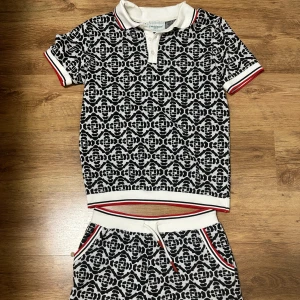 Casablanca  - Casablanca piké t-shirt med svartvitt grafiskt mönster, ribbade muddar och krage med röda och svarta ränder. Klassisk pikéknäppning och sportig vibe. Perfekt för dig som gillar statement-plagg och snygga detaljer.