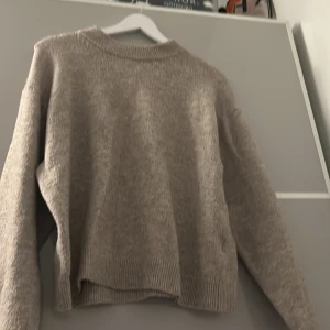 Beige stickad tröja med lång ärm - Mysig beige stickad tröja med rund halsringning och långa ärmar. Tröjan har ribbade muddar vid ärmslut och nederkant, vilket ger en avslappnad och skön känsla. Perfekt för lager-på-lager under kyliga dagar.