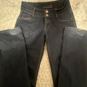 Mörkblå jeans från Dromedar - Snygga mörkblå jeans från Dromedar med klassisk femficksdesign och kontrastsömmar. Jeansen har dubbla knappar i midjan och läderpatch bak. Raka/utsvängda, säljer de för de är för långa för mig hade passat nån som är minst 168 lång 