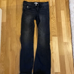 Svarta jeans med bootcut och fickdetaljer från gina tricot - Snygga svarta jeans med lätt tvättad look och bootcut-ben. Byxorna har framfickor med knappdetaljer och bakfickor med lock och silverfärgade knappar. Klassisk femficksmodell i stretchigt jeanstyg, perfekt till en avslappnad stil.