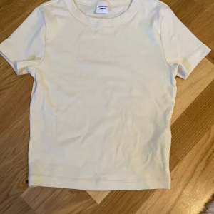 Vit basic t-shirt från Gina Tricot - Enkel och fräsch vit t-shirt från Gina Tricot. Modellen är kortärmad med rund halsringning och har en tight passform. Tillverkad i mjuk bomull som känns skön mot huden. Perfekt att matcha med jeans eller shorts för en clean look. Har ett litet hår vid armen men syns inte så mycket💛