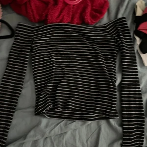 Randig offshoulder topp från Noisy May - Svart ribbad offshoulder topp från Noisy May med vita tunna ränder. Långärmad och figurnära passform, perfekt att styla med jeans eller kjol. Mjuk och stretchig känsla, passar dig som gillar en enkel men snygg look.