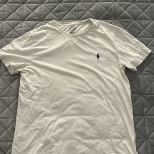 Vit t-shirt från Polo Ralph Lauren - Klassisk vit t-shirt från Polo Ralph Lauren med broderad marinblå logga på bröstet. Modellen är custom slim fit med rund hals och korta ärmar. Tillverkad i mjuk bomull som känns skön mot huden. Perfekt för en clean och stilren look.