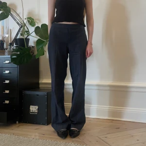 Mörkblå byxor - Mörkblå tygbyxor med lite vitt i väven. Aningen stora på mig som är storlek 34, uppskattar att de är storlek 36 🫶🏻 De har dragkedja i ena sidan och veck på benen framtill, supersnygga! 💕Har passform som ett par kostymbyxor men tunt och somrigt material 💕