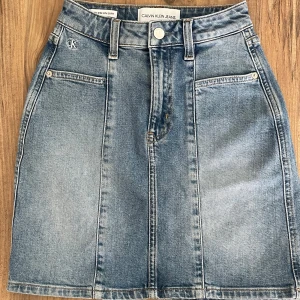 Blå jeanskjol från Calvin Klein - Snygg blå jeanskjol från Calvin Klein med klassisk femficksdesign, bälteshällor och CK-logga framtill. Kjolen har en rak passform och är i en ljus tvättad denim som ger en cool och avslappnad vibe. Perfekt att matcha med sneakers eller boots.