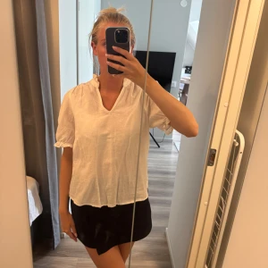 Vit blus i linne från Neo Noir - Superfin vit blus från Neo Noir i luftigt linne. Blusen har korta puffärmar med resår och en liten volangkant vid halsen. V-ringad och avslappnad passform, perfekt till både jeans och kjol. Enkel men ändå söt design som passar året runt.