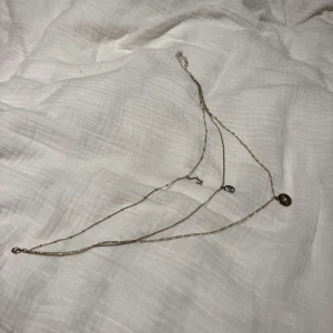 Layered halsband med stjärntecken - Snyggt lager-på-lager halsband i silverfärg med tre olika hängen: ett runt med stjärndetalj och två med stjärnteckenmotiv, varav ett är inramat i en cirkel. Kedjorna har olika strukturer och ger en trendig look. Perfekt för dig som gillar astrologi och unika smycken.