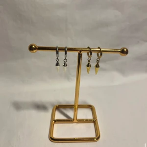 Örhängen med konformade hängen - Två par örhängen med konformade hängen, ett par i silverfärg och ett par i guldfärg. Båda har minimalistisk design med små ringar och spetsiga hängen som ger en edgy vibe. Perfekta för att lyfta din stil med en cool detalj.