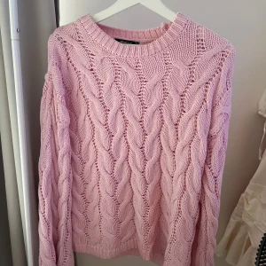 Rosa stickad tröja från Gina Tricot - Supersöt rosa stickad tröja från Gina Tricot i storlek XS. Tröjan har ett chunky flätmönster, rund halsringning och långa ärmar. Perfekt för att ge din outfit en mysig och trendig vibe. Oversized