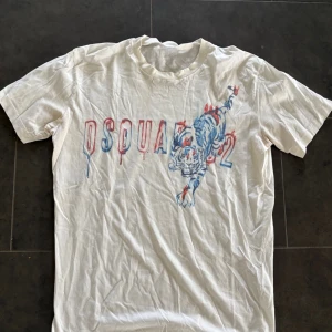 Vit Dsquared2 t-shirt med tigertryck - Snygg vit t-shirt från Dsquared2 med coolt tigertryck i blått och rött framtill samt DSQUARED2-logga. Klassisk passform och rund hals. Perfekt för dig som vill sticka ut med en unik printad tee.