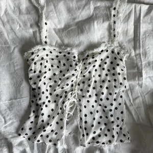 Prickig vit snörad linnetopp - Jättesöt prickig topp. Köpt secondhand men aldrig använt själv, i fint skick. Storlek M men liten i storleken. Skulle säga att den passar S/XS bättre! Har en liten fläck på baksidan, men syns nästan inte och täcks av håret ifall man har utsläppt😇🫰🏼🫰🏼