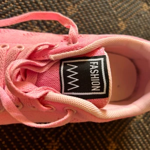 Rosa sneakers med mesh och snörning - Säljer ett par snygga rosa sneakers från Fashion i storlek 39. Skorna har ventilerande meshdetaljer, klassisk snörning och vit sula med rosa detaljer. Perfekta för dig som gillar färg och vill sticka ut lite extra.