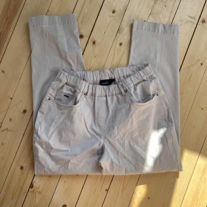 Beige byxor med resårmidja från LauRie - Snygga beige byxor från LauRie med resår i midjan för extra komfort. Klassisk femficksmodell med raka ben och diskreta sömdetaljer. Perfekta för en chill och stilren look, lätta att matcha med det mesta.