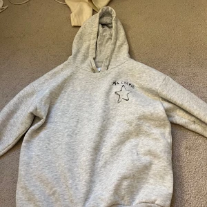 Grå hoodie Ma Chérie Gina Tricot - Ljusgrå hoodie från Gina Tricot med svart texten 'Ma Chérie' och en stjärna tryckt både fram och bak. Tröjan har huva med snörning och är långärmad. Perfekt för dig som gillar en chill och enkel stil. Nästan aldrig använd.