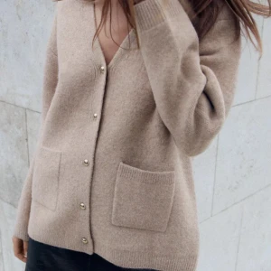 Beige kofta i  med guldknappar - Supermjuk beige kofta med snygga guldknappar framtill och två stora fickor. Koftan har v-ringning, lång ärm och en loose fit som ger en chill vibe. Perfekt att slänga över en t-shirt eller ha som lager på lager under kyliga dagar. Jättesnygg och känns som en i mängden!!  Tveka inte över att höra av dig vid frågor:)