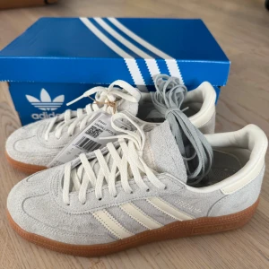 Adidas Handball Spezial W ljusgrå sneakers - Adidas Handball Spezial W sneakers i ljusgrå mocka med vita detaljer. Skorna har en snygg gummisula och levereras med både vita och grå skosnören.  Perfekt för dig som gillar retrostil och streetwear. Dem är endast testade utomhus en gång.                                         Nypris är 1250kr 