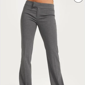 Grå kostymbyxor med bootcut - Snygga grå kostymbyxor med låg midja. Byxorna har en stilren look med dold knäppning framtill💕Den är lite nopprig💕