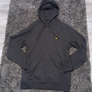 Mörkgrå hoodie från Lyle & Scott S - Säljer en mörkgrå hoodie från Lyle & Scott i storlek S. Klassisk modell med huva, snörning och känguruficka framtill. Liten gul logga på bröstet. Perfekt för chill dagar och enkel att matcha med jeans eller joggers. Har runt 3 väldigt små vita fläckar som jag tror går bort i tvätten men syns inte mycket alls. Kom med bud eller förslag. 
